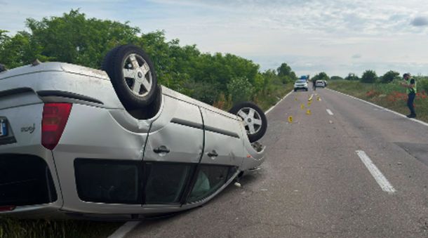White SUV flipped onto its roof on a rural two-lane road; emergency responders and traffic cones visible in the distance.