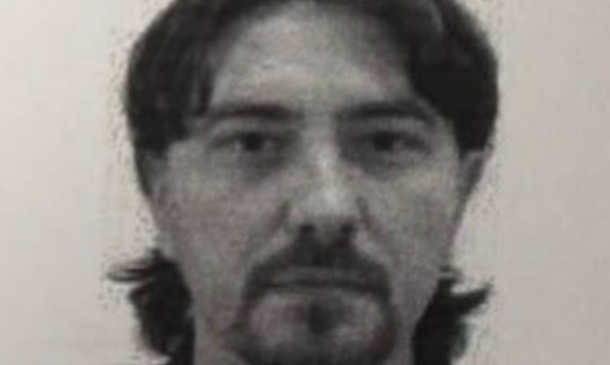 Black-and-white headshot of a man with medium-length dark hair and a goatee, wearing a dark collared shirt, looking at the camera.
