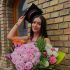 Graduate woman wearing a cap and gown holding a large bouquet of pink and white flowers outside a brick building.