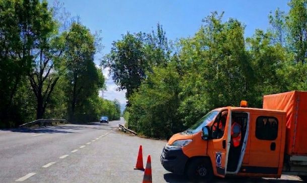 Orange maintenance van with open door parked on a tree-lined road, orange traffic cones in front signaling work ahead.