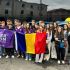 Group of students posing in front of a bus, holding a purple 'Cyber Moon' banner and a Romanian flag.