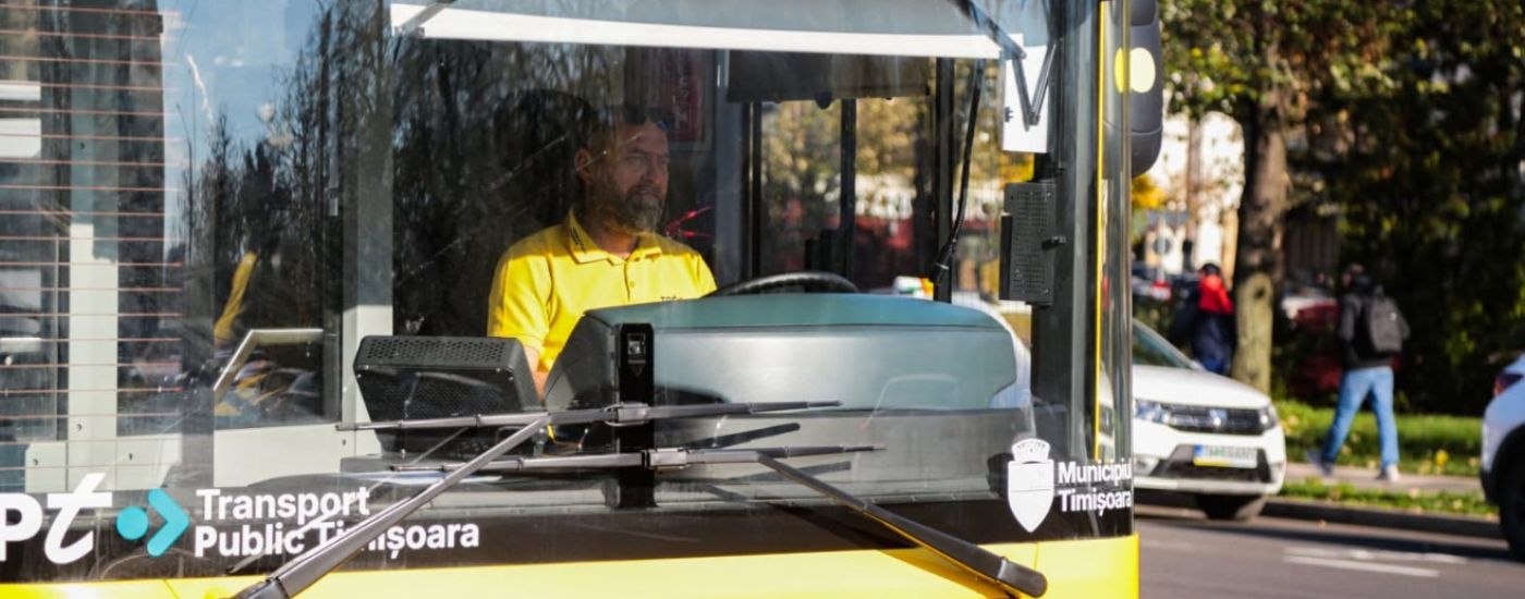 Public transit bus front view with a driver in a yellow shirt; Timisoara branding and accessibility icons on the bumper.