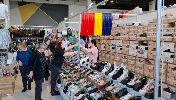Shoppers browse a busy shoe stall inside a store; rows of sandals and sneakers line the displays with stacked shoeboxes in the background.