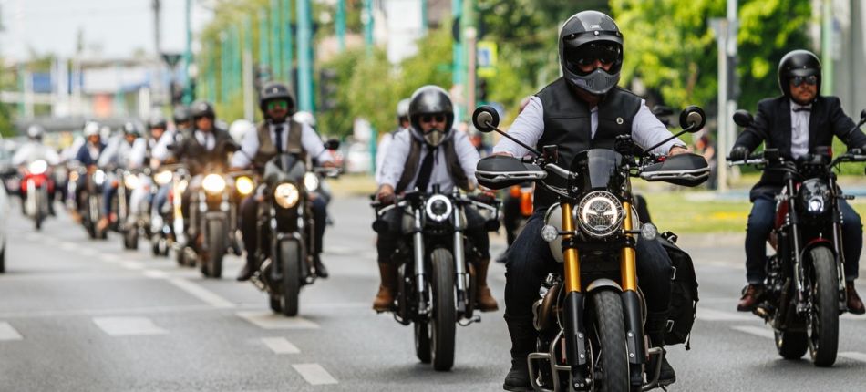 Group of motorcyclists riding down a city street, front rider wearing a black helmet and vest.