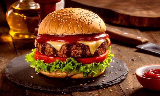 Juicy hamburger with sesame bun, melted cheese, beef patty, lettuce and tomato on a dark slate plate.
