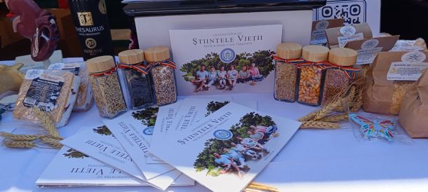 Table display of grain packets and glass jars with ribbons, plus brochures and a university poster in the background.