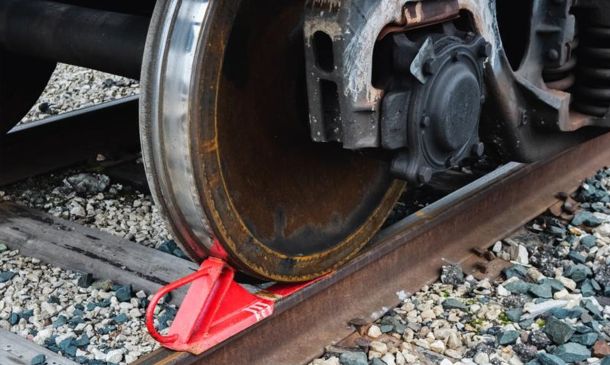 Close-up of a train wheel resting on the rail, with a red wedge wheel chock securing it