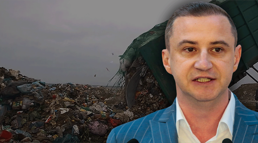 Man in a blue pinstripe suit speaking at a press conference with a landfill and garbage mound in the background.