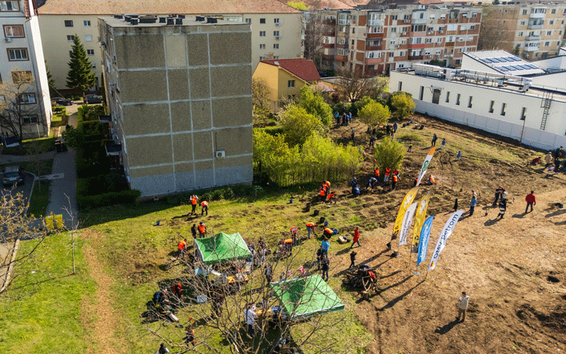 Aerial view of a community event in a courtyard: people gather around two green canopy tents near apartment buildings with banners nearby.