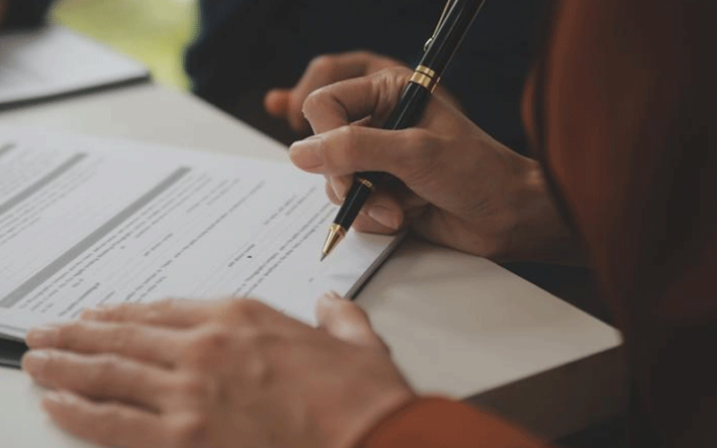 Person signing a document with a black and gold pen at a white desk.
