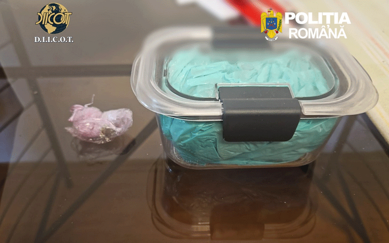 Clear evidence container with a teal bag inside on a glass table; a small pink bag sits to the left; DIICOT and Romanian Police logos in the corner.
