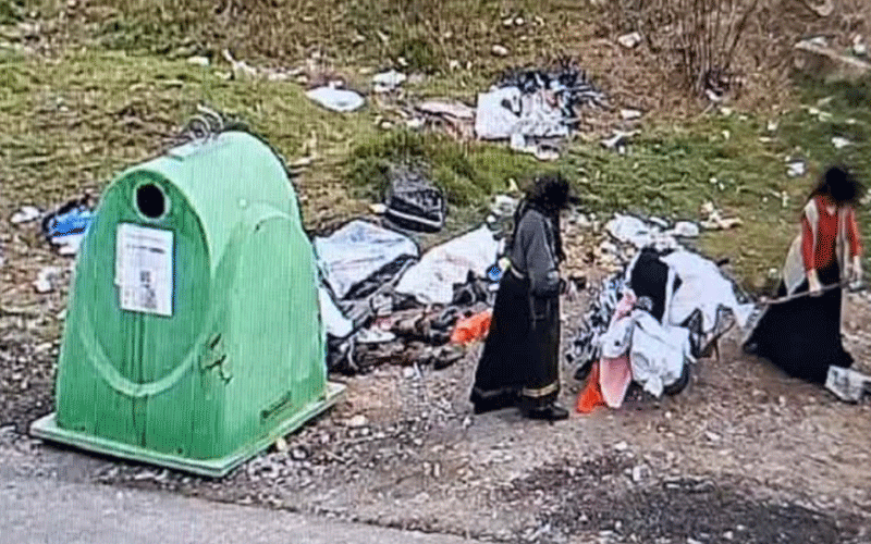 Green recycling/bin near a litter pile with two people sorting through trash by the roadside attached to a grassy area.
