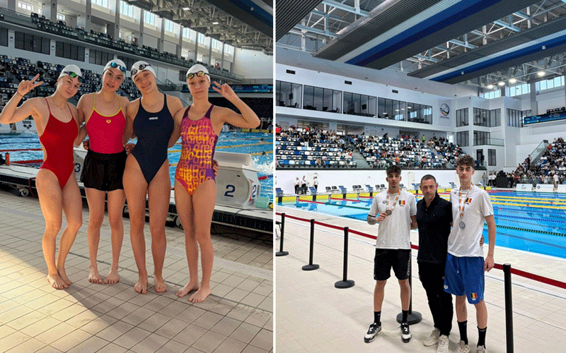 Group of four female swimmers in swimsuits and caps posing by an indoor pool after a race.