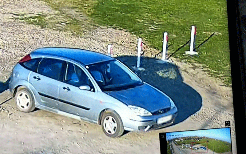 Silver hatchback parked on a dirt lot with white posts and green grass nearby.