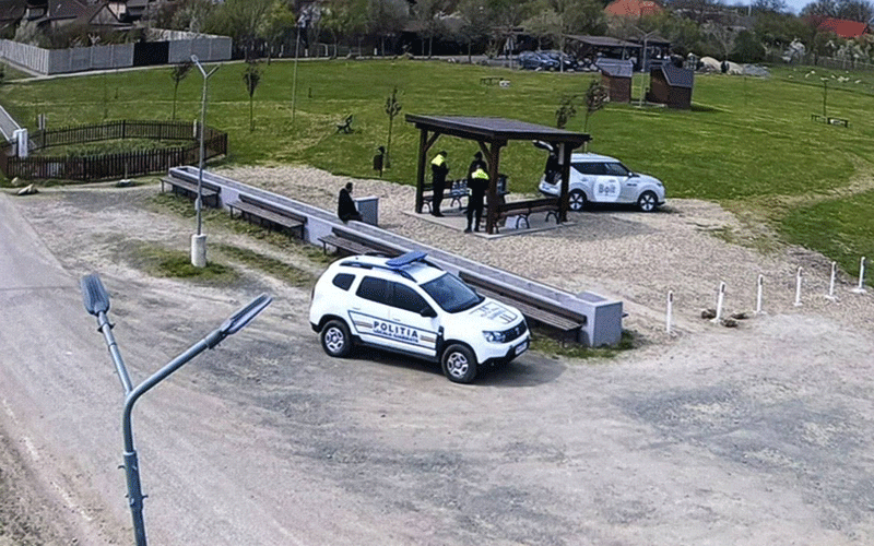 White police SUV parked on a gravel area near benches and a small shelter with people nearby in a park setting