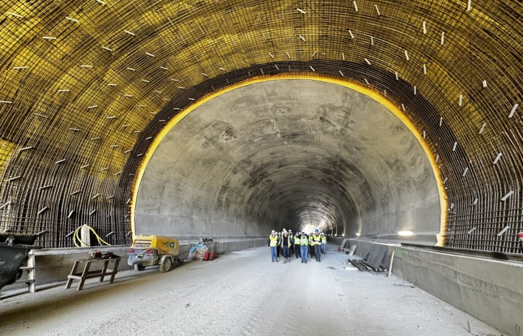 Group of construction workers in hard hats and high-visibility vests standing inside a large tunnel under construction.