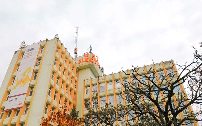 Large peach-colored multi-story campus building with many windows, a tall banner on the left wall, and leafless trees in the foreground.