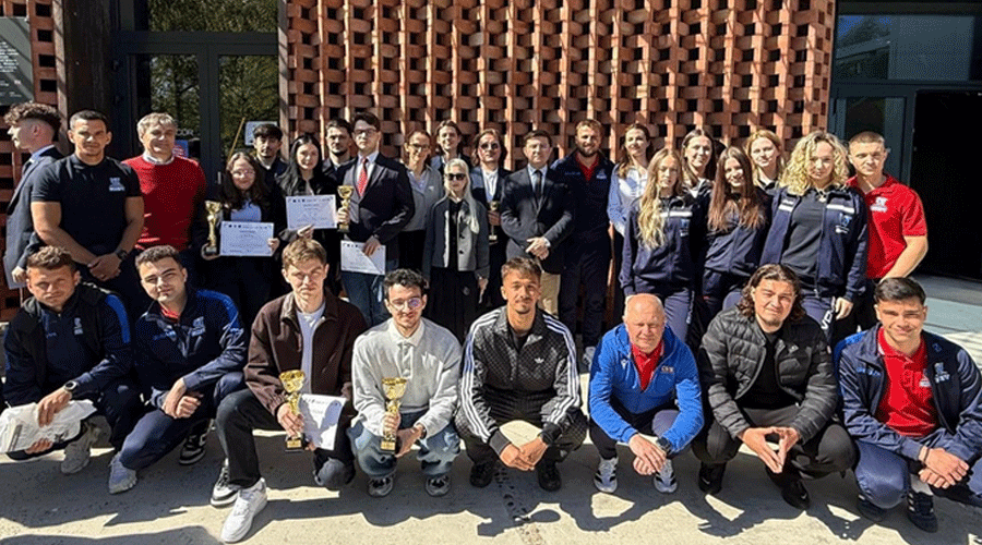 Group of young athletes and coaches posing outside a building, several holding trophies and certificates.