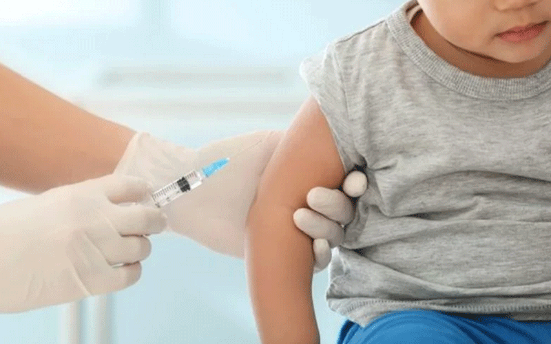 Child receives a vaccination in the upper arm from a healthcare professional wearing gloves.