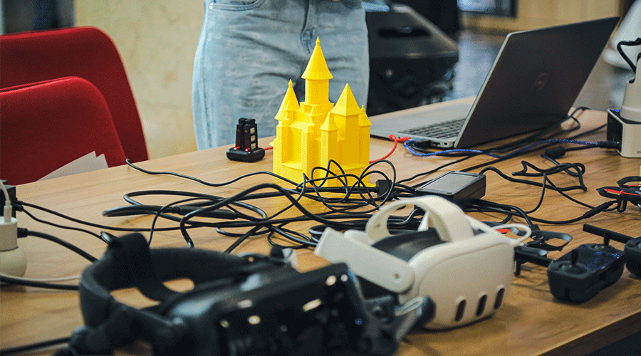 UVT-laboratoare-7 - Sursa de Vest Tangled desk with cables and a bright yellow castle model beside a laptop and headset on a cluttered worktable