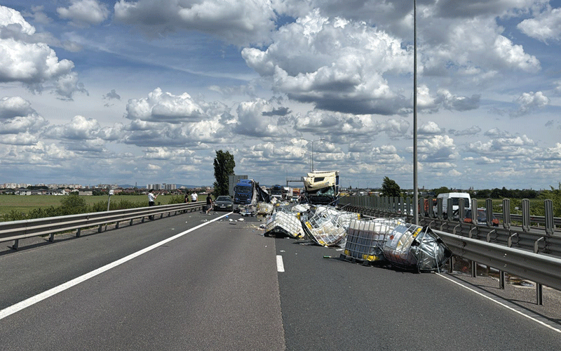 accident-autotrenuri-a1 - Sursa de Vest Highway crash scene with a toppled truck and scattered cargo blocking the road; onlookers and emergency responders nearby on a cloudy day.