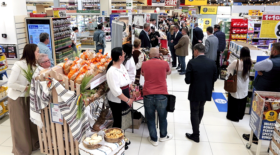 Crowded indoor market or store with a pastry stand and shoppers browsing nearby shelves.