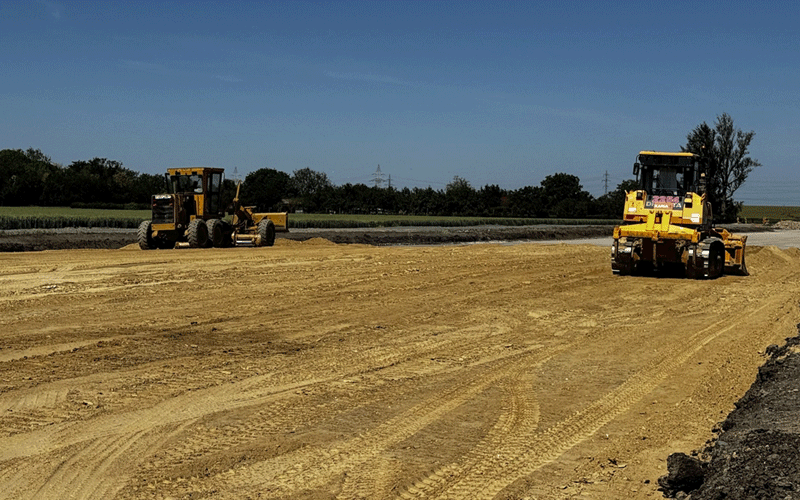 centura-vest2 - Sursa de Vest Two yellow heavy machines working on a dirt road at a construction site under a clear blue sky.