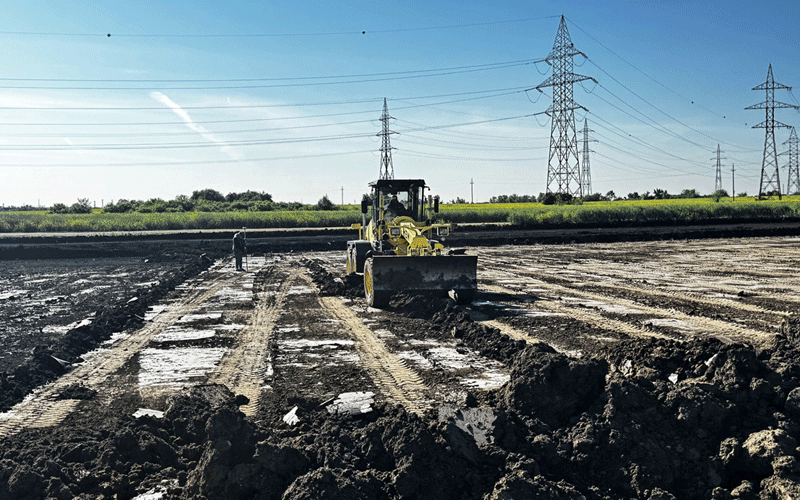 centura-vest3 - Sursa de Vest Bulldozer smoothing a muddy construction site with a worker nearby; power lines and transmission towers in the distance.
