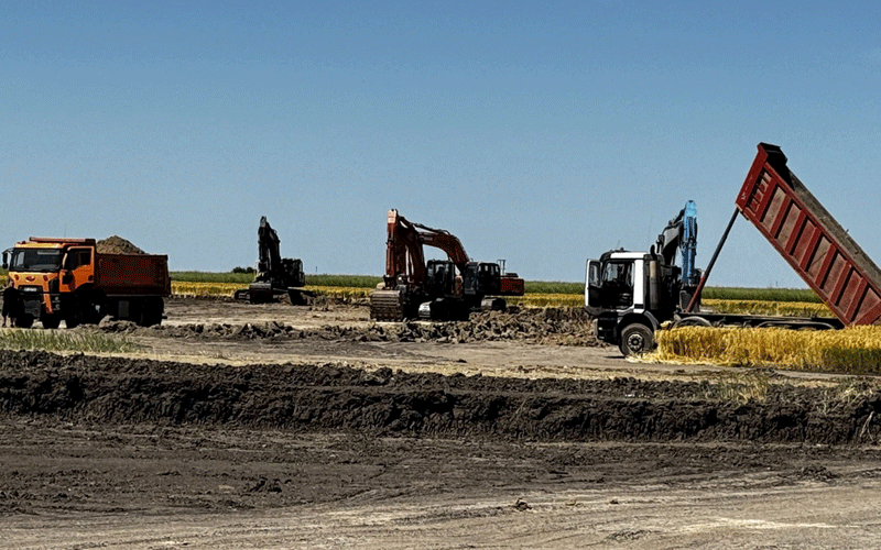 centura-vest7 - Sursa de Vest Construction site with a dump truck and several excavators working on dirt under a blue sky.