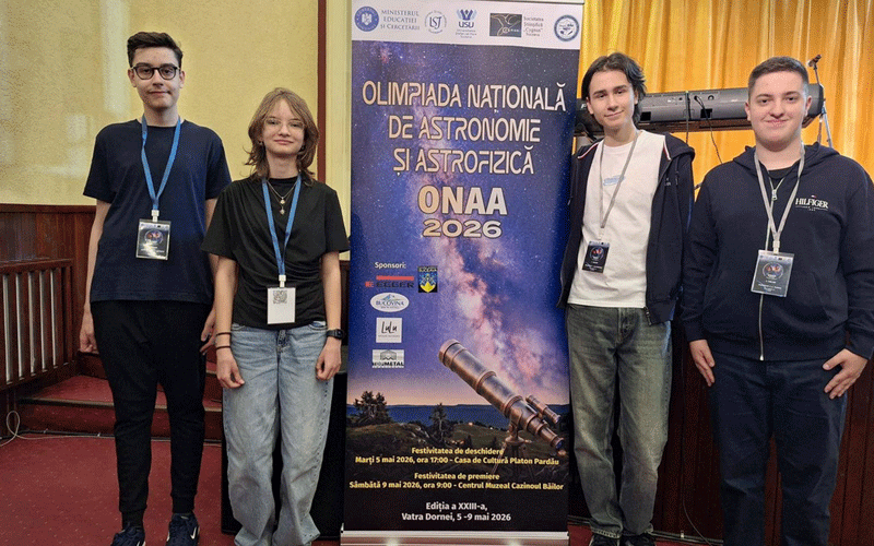 Four young participants stand beside a vertical banner for ONA A 2026 Astronomy and Astrophysics Olympiad, with a telescope image at the bottom and event logos above them (indoor stage setting).