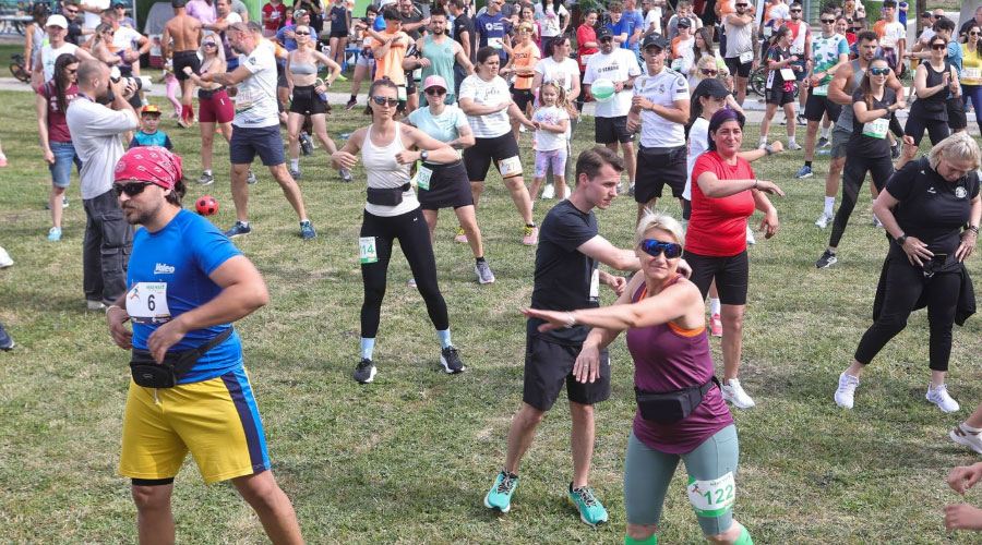 Crowd of runners warming up on a grassy field before a race; participants wear bib numbers and athletic wear.