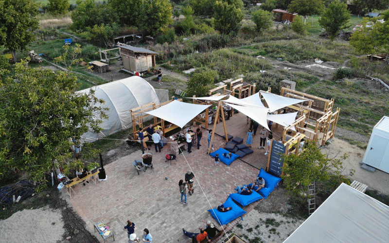 Aerial view of an outdoor event with white shade sails, wooden deck, and people mingling among blue bean bags and tables.