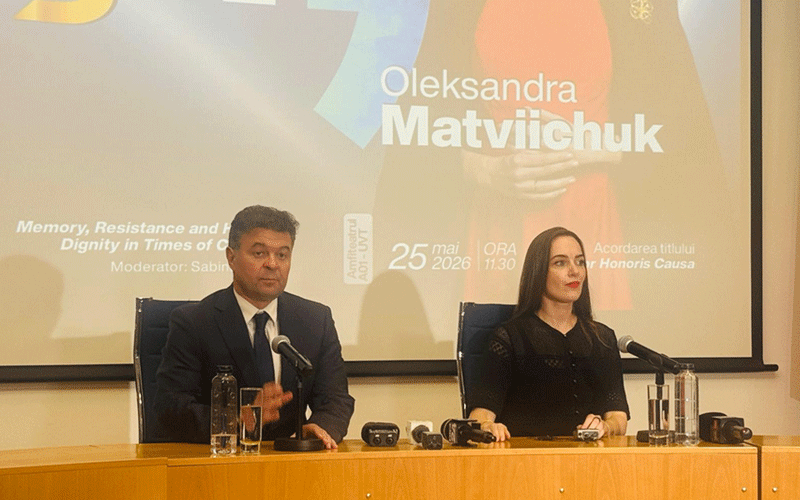 Two panelists sit at a wooden table with microphones during a press conference; projection behind shows Oleksandra Matvichuk's name and event details
