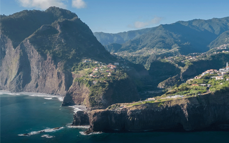 Steep coastal cliffs with a village perched on the edge, overlooking the blue sea.