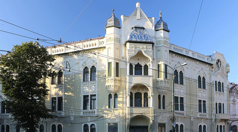 Historic pale-yellow building with ornate white detailing and arched balconies against a clear blue sky