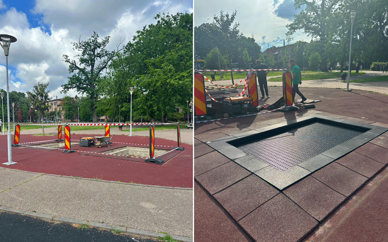 Park construction area with red surface, yellow striped barriers, and an open pit ready for repairs; equipment nearby.
