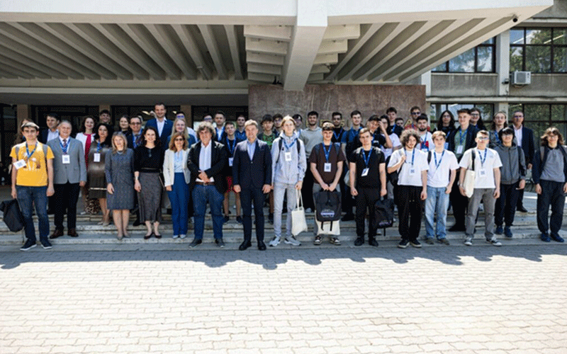 Group of diverse students and professionals with badges posing on stairs outside a modern building.