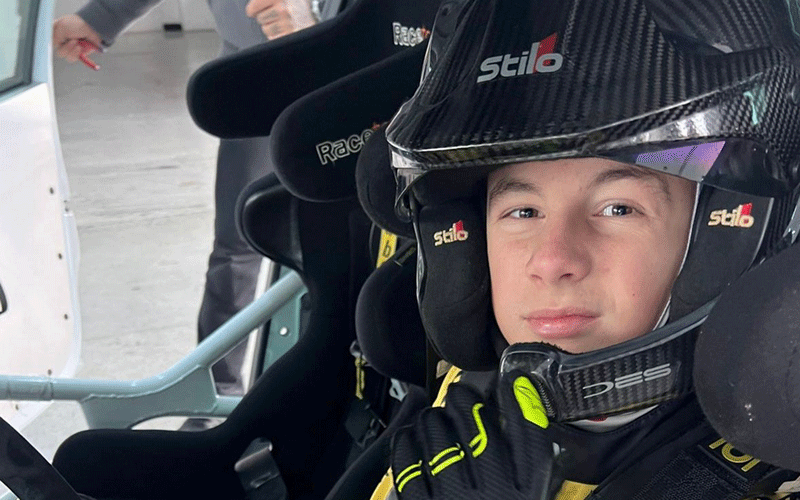 Young race car driver wearing a black Stilo helmet seated in a race car with bucket racing seats.