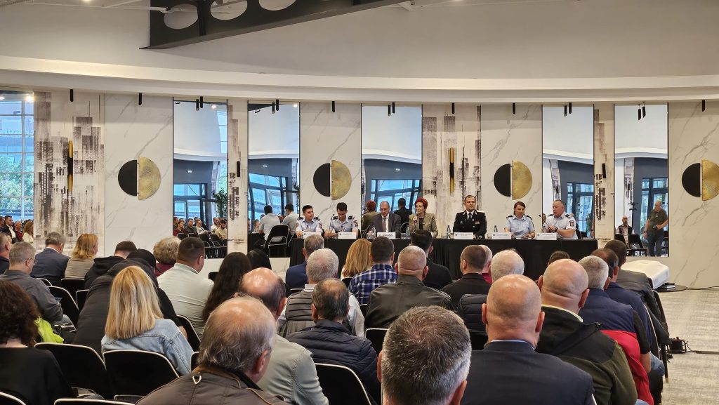 Panel of uniformed officials seated at a long table on a stage, addressing a large audience in a conference hall.