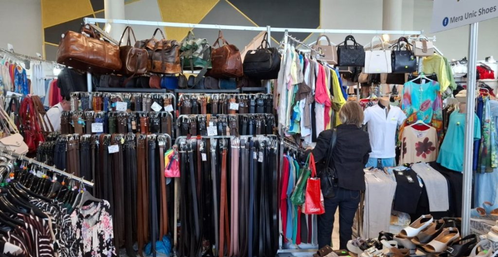 siu 1 - Sursa de Vest Clothing and accessories stall with racks of belts, handbags, and garments at a market booth.