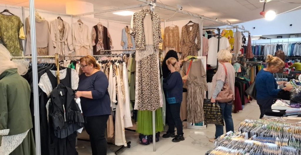 siu 5 - Sursa de Vest Busy clothing market stall with racks of dresses and shoppers browsing.