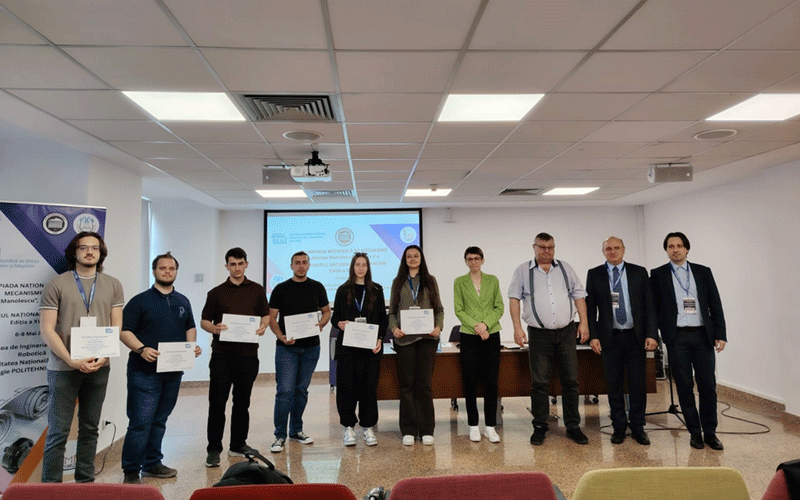 Ten people stand on a stage in a conference room, each holding a certificate during an awards ceremony with a projector screen behind them.