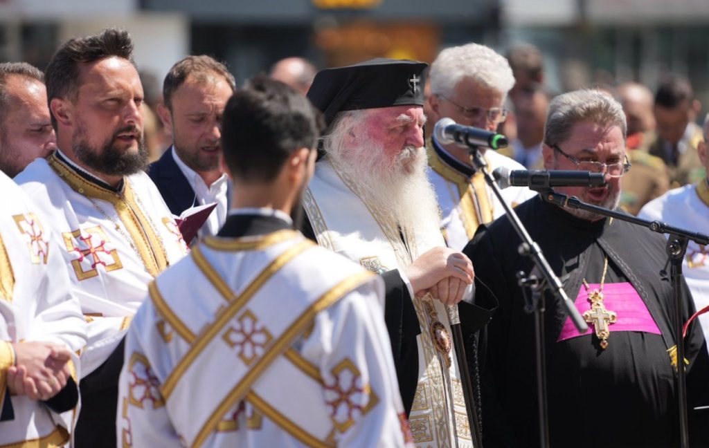 ziua eroilor 6 - Sursa de Vest Orthodox clergy in white and gold robes gathered outdoors, some singing or praying around a microphone.