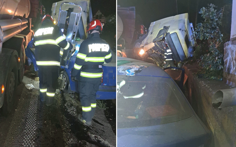 Nighttime crash scene with firefighters in reflective gear around a tipped blue truck wedged against a curb, a tanker truck nearby.