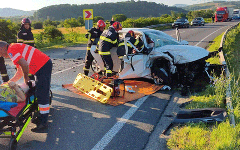 Emergency responders stretch a casualty on a stretcher beside a white damaged car on a highway after a crash
