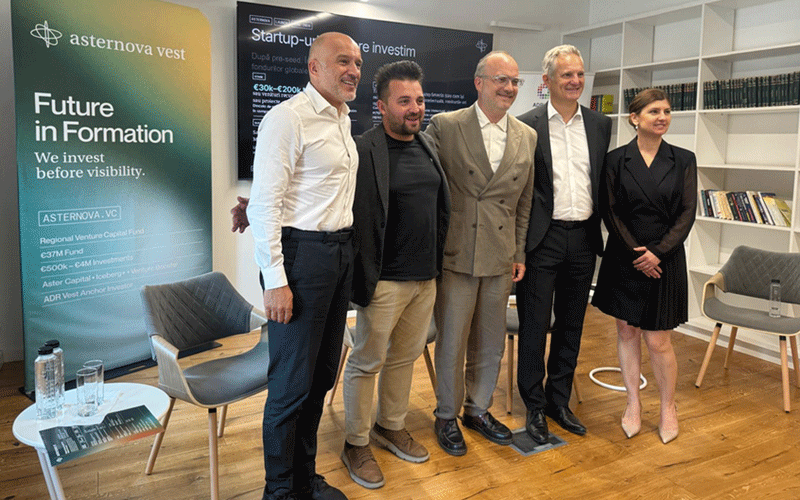 Five professionals pose for a group photo in a modern office during a venture event; banners read 'Future in Formation' and 'Startup'.