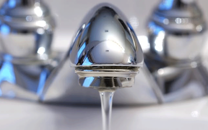 Close-up of a polished chrome faucet spout with a single droplet of water falling from it