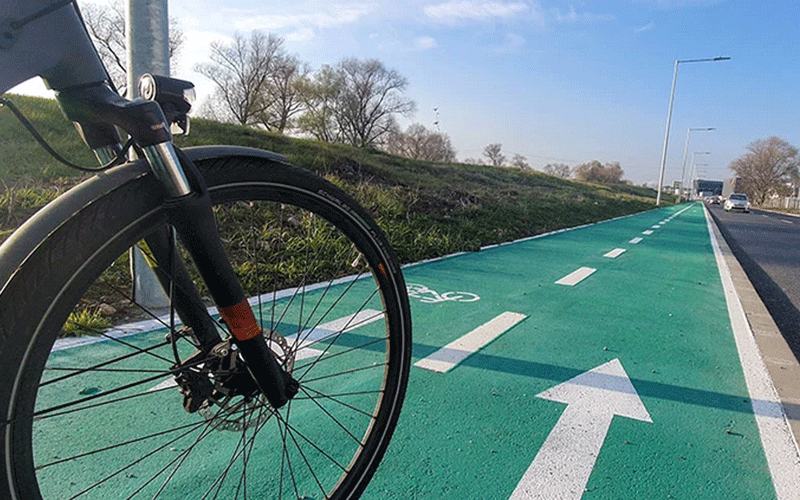 Front wheel of a bicycle in a green bike lane with a large white forward arrow, road in the distance.