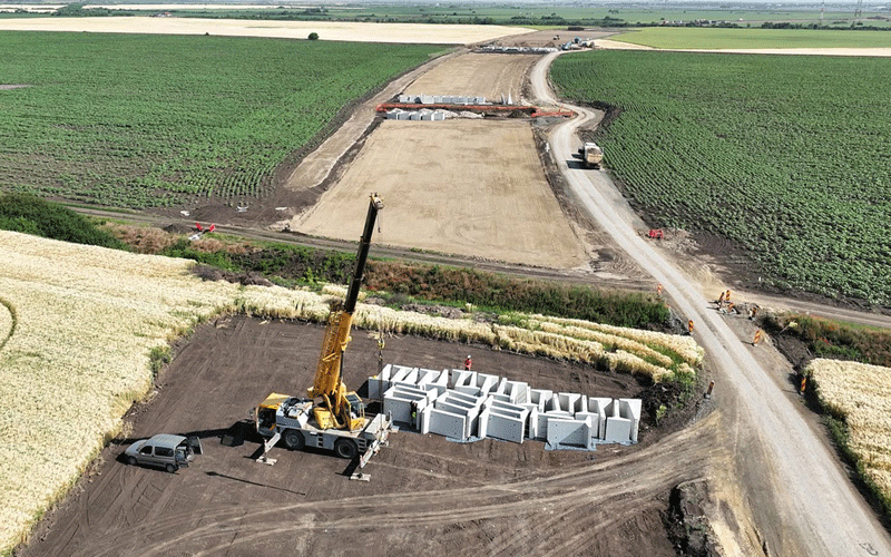 centura-vest2 - Sursa de Vest Construction site in a rural field with a yellow crane lifting concrete blocks into a storage area.