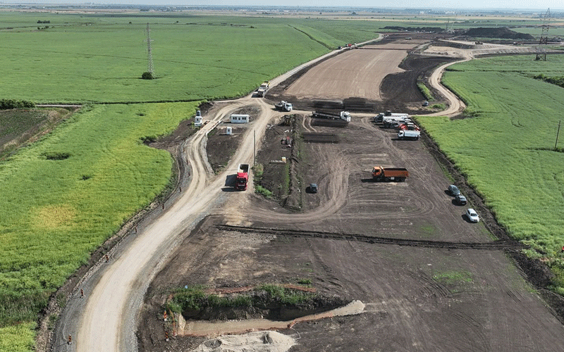 centura-vest3 - Sursa de Vest A construction site in a rural area with dirt roads and multiple trucks and equipment grading earth among green fields.